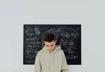 boy standing in front of a blackboard with equations written on it
